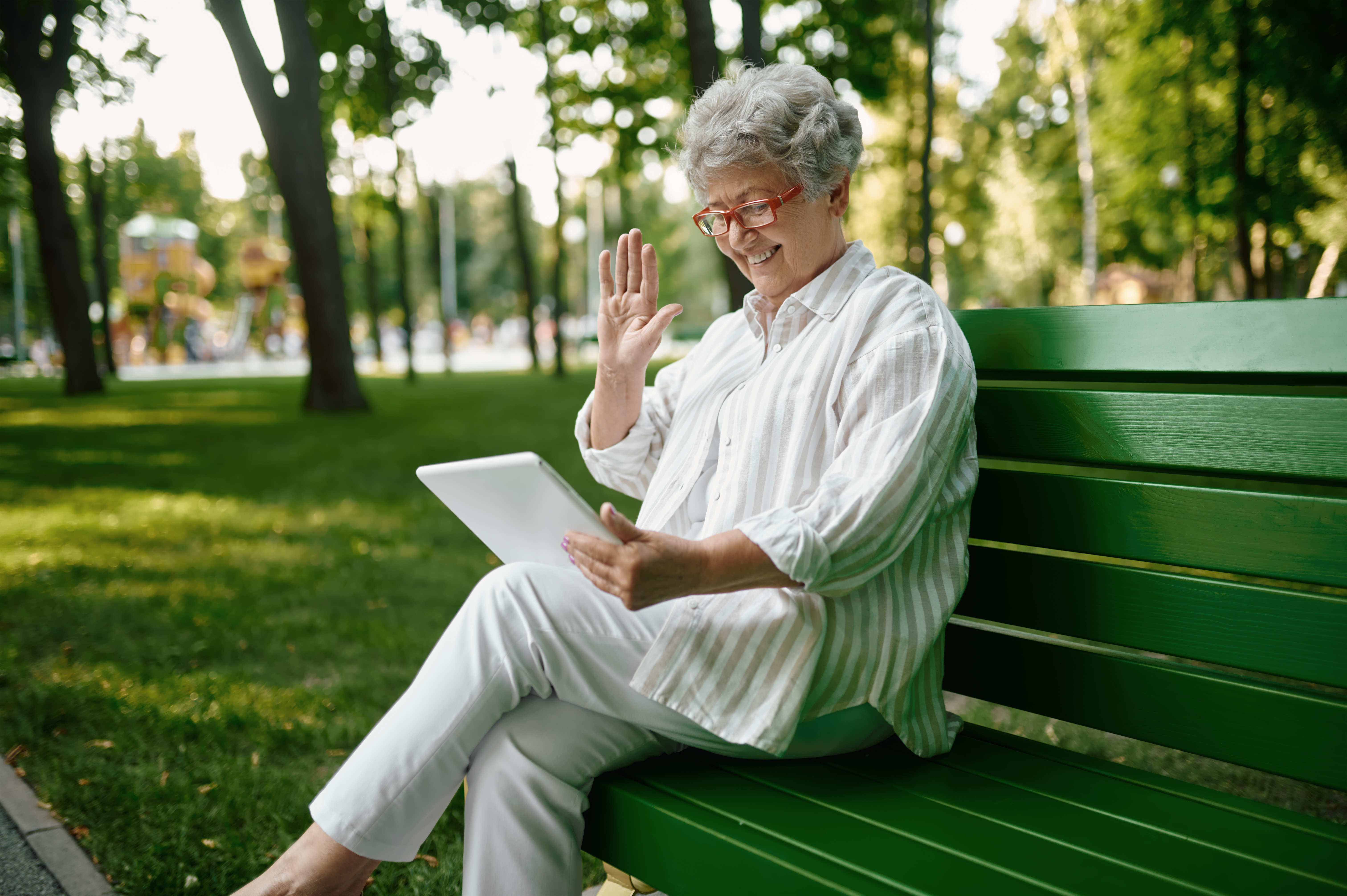 Mujer sentada en el banco de un parque sujetando una tablet