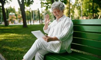 Mujer sentada en el banco de un parque sujetando una tablet